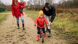 Happy family walking outdoors in fall, teaching child to ride bike.
